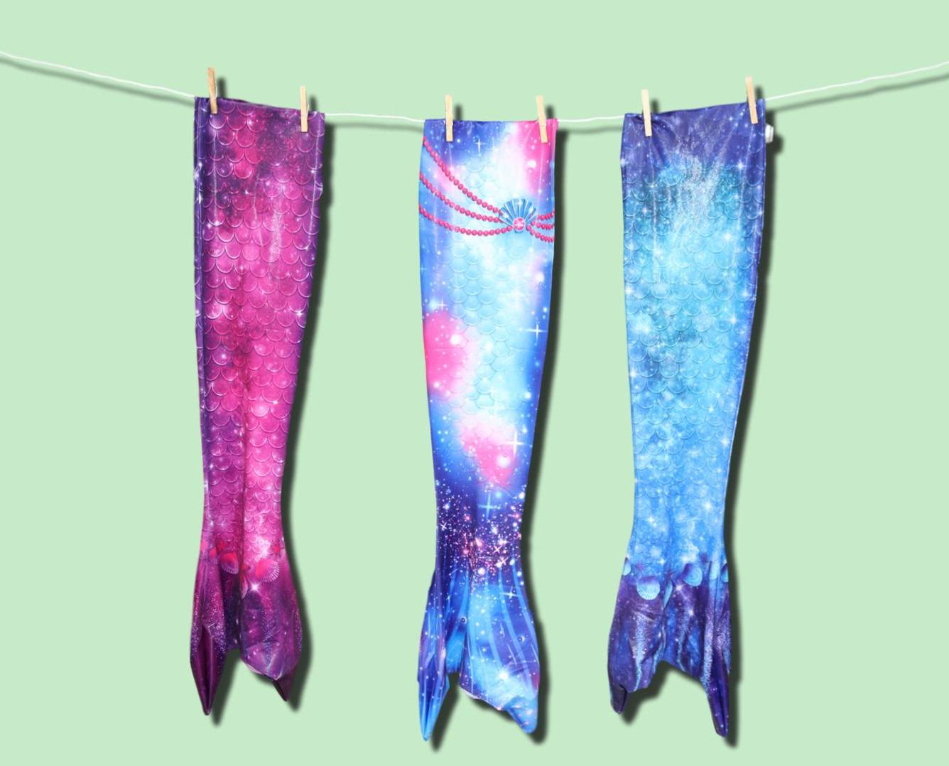 Drie kleurrijke zeemeerminstaarten hangend aan een waslijn tegen groene achtergrond